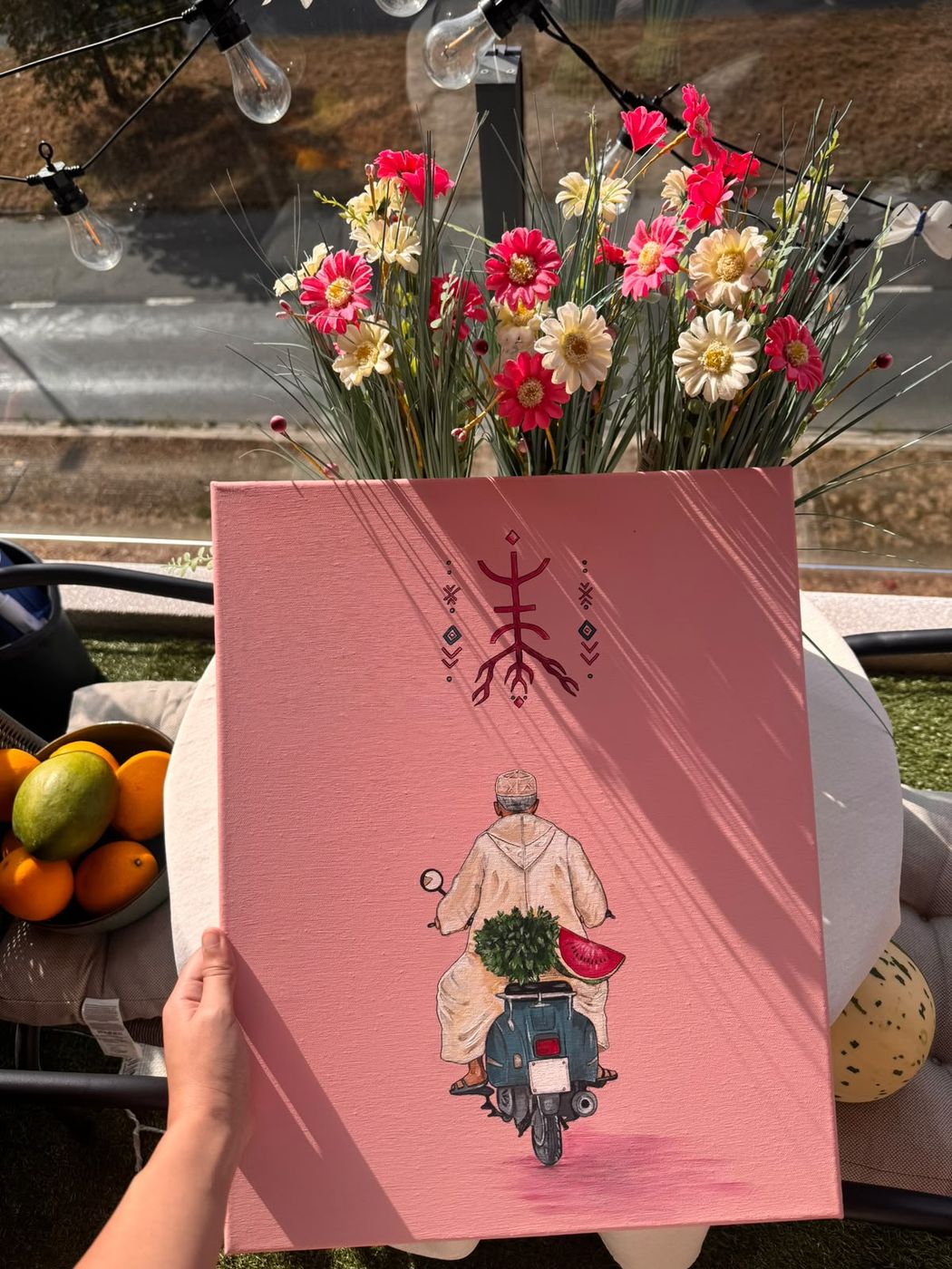La toile rose La mobylette de Jeddi II tenue à la main, derrière un bouquet de fleurs
